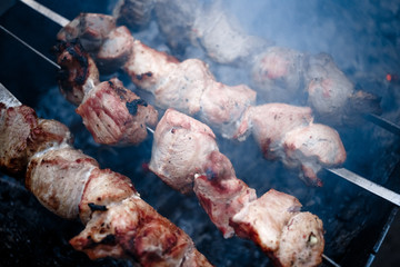 Grilled kebab cooking on metal skewers (grill). Roasted meat cooked at barbecue with smoke. Close up BBQ fresh pork meat chop slices. Traditional eastern dish, shish kebab.