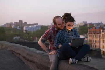 Fototapeta na wymiar Busy working female. Couple distraction. Modern hipsters on roof, social media activity outdoors. Freelance with laptop, urban background