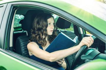 Naklejka premium Woman driver reading a book in the car. Distracted and dangerous driving. The traffic violation.