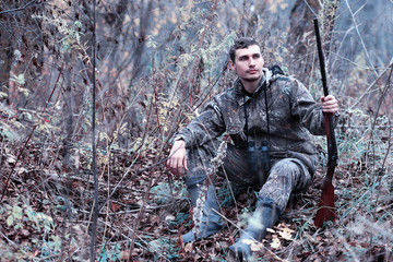 A man in camouflage and with a hunting rifle in a forest on a spring hunt