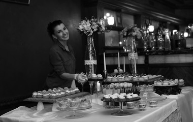 table with sweets and a variety of sweet snacks against the backdrop of  a girl confectioner