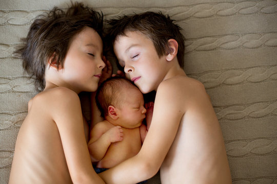 Two children, toddler and his big brother, hugging and kissing their newborn baby brother at home