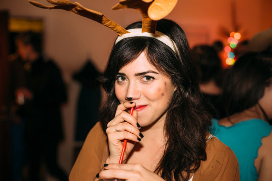 Young Smiling Brunette Woman Dressed As Reindeer Holding Straw And Drink At Christmas Party