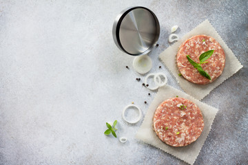 Raw hamburgers - cutlets from organic beef meat with spices and basil on a stone or slate background, top view with copy space.