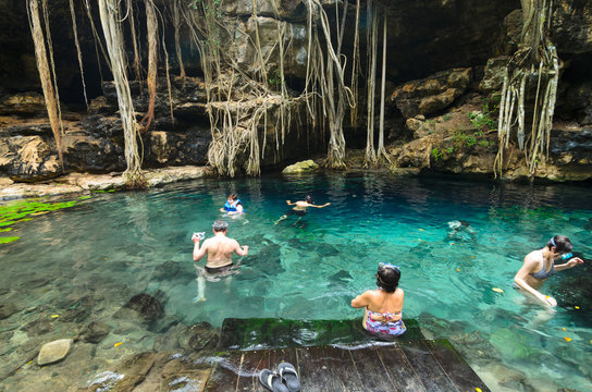 People swimming in transparent turquoise water of cenote