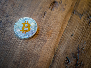 Silver bitcoin with cold details on rustic wood background.