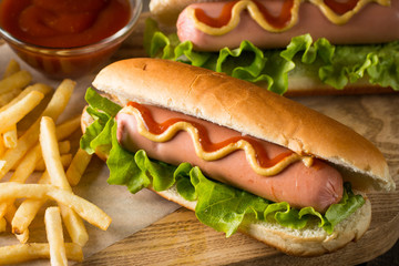 Tasty barbecue grilled hot dog with salad,yellow mustard, onion, ketchup, and French fries on wooden background. Junk and fast food concept.