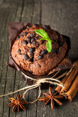 chocolate dark muffin with a leaf of mint on a wooden table with cinnamon, anise, chocolate