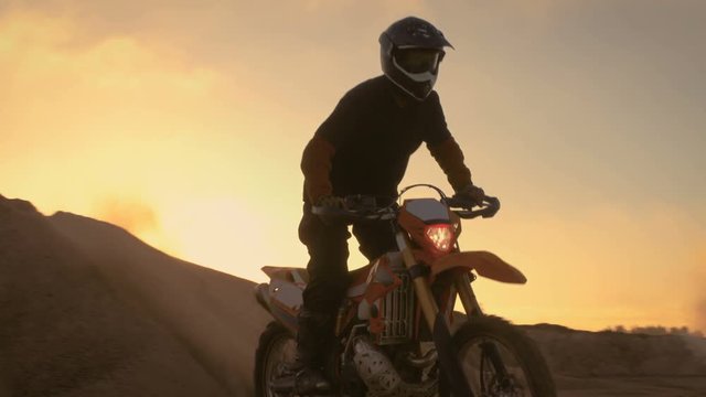 Professional Motocross Motorcycle Rider Drives on the Dune and Stops on the Top. It's Sunset Time and Track is Covered with Smoke/ Mist. Shot on RED EPIC-W 8K Helium Cinema Camera.