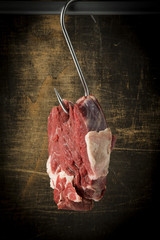 rohes Stück Rindfleisch am Haken, hängend vor dunklem Hintergrund