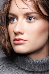 Fototapeta premium Beauty portrait of young woman in gray wool sweater. Brunette girl with bright blue eyes and day female makeup