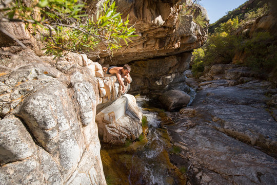 Relaxed man lies on rock watching river flow beneath him at rockpool