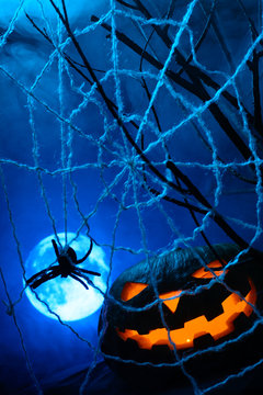 Scary Halloween pumpkin with a glowing face and a cobweb with a spider on the background of the full moon in the fog