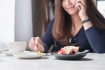 Closeup image of a smiley beautiful Asian woman holding and talking on smart phone with white coffee cup and dessert plates on wooden table in vintage cafe