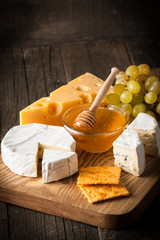 Slate board with various cheese and a glass of red rose wine. Brie. Camembert. Gouda, Masdaam, Roquefort, Cheddar and grapes on a wood with nuts, honey, crackers, blue cheese. Italian, French cheese.