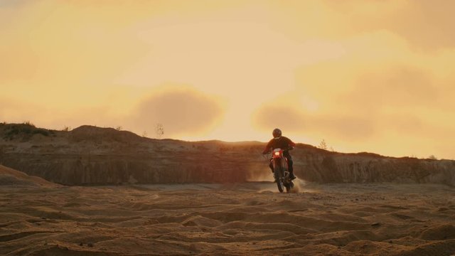 Professional Motocross Motorcycle Rider Drives Over the Dune and Further Down the Off-Road Track. It's Sunset and Track is Covered with Smoke/ Mist. Shot on RED EPIC-W 8K Helium Cinema Camera.