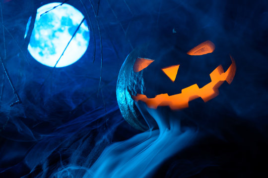 Scary Halloween pumpkin with glowing face on the background of the full moon in the fog