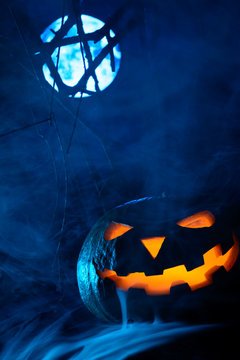 Scary Halloween pumpkin with glowing face on the background of the full moon in the fog