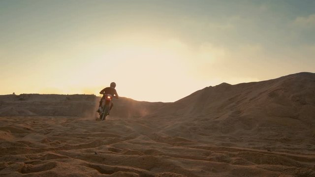 Professional Motocross Motorcycle Rider Driving Over the Dune and Further Down the Off-Road Track. It's Sunset and Track is Covered with Smoke/ Mist. Shot on RED EPIC-W 8K Helium Cinema Camera.