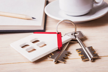 House model with keys over defocused sketchbook and coffee cup