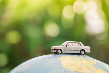 Travel and transport concept. Miniature Toy car on world map balloon with green nature as background.