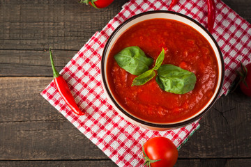 Chili tomato soup with sour cream sauce, cottage cheese, basil and red hot peppers on wooden background. Healthy, vegan and dieting lunch and dinner concept.