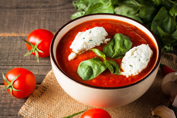 Chili tomato soup with sour cream sauce, cottage cheese, basil and red hot peppers on wooden background. Healthy, vegan and dieting lunch and dinner concept.