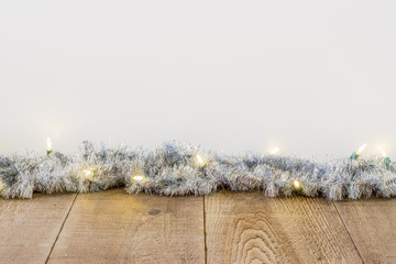 Tinsel with white Christmas lights along edge of rustic plank surface, white background