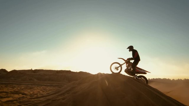 Professional Motocross Motorcycle Rider Jumping Over the Dune and Further Down the Off-Road Track. Shot on Deserted Quarry while Sun is Setting. Shot on RED EPIC-W 8K Helium Cinema Camera.