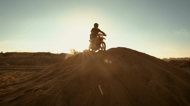 Professional Motocross Rider on FMX Motorcycle Drives on the Sand Dune and Stops There to Admire Scenic Sunsetting View. Shot on RED EPIC-W 8K Helium Cinema Camera.