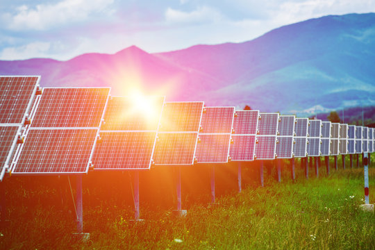 Panels Of The Solar Energy Plant Under The Blue Sky With White Clouds With Sun Flare Hitting The Surface - Clean Energy Concept