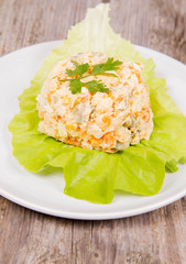 Vegetable salad (potato, carrot, corn, pea, egg, leek) with mayonnaise on a wooden background