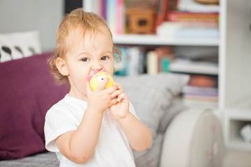 One and a half year old toddler baby girl sucking her toys in the living room