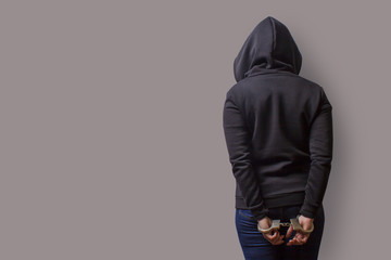 rear view of a girl in a black hood with handcuffed hands isolated on a gray background