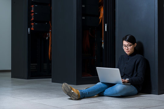 Female technician using a laptop while sitting in data center