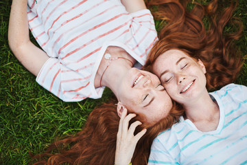 Twin ginger girls caring about each other, having fun on a sunny summer day in park. Listening to...