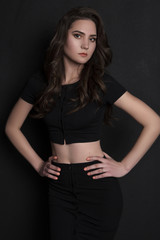 brunette girl in black clothes standing looking at camera black background