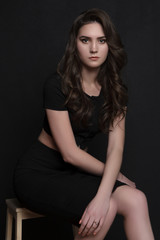 Naklejka premium portrait of a beautiful girl in black clothes sitting dark background