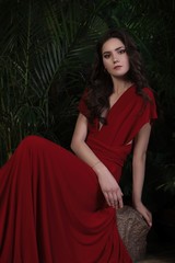 Fototapeta na wymiar brunette girl in red dress sitting among tropical leaves