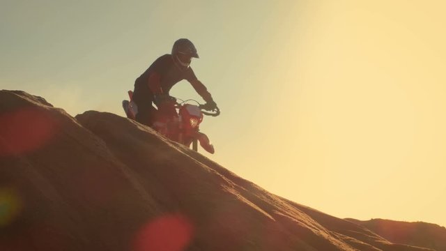 Professional Motocross Motorcycle Rider Drives Over the Dune and Further Down the Off-Road Track. It's Sunset. Shot on RED EPIC-W 8K Helium Cinema Camera.