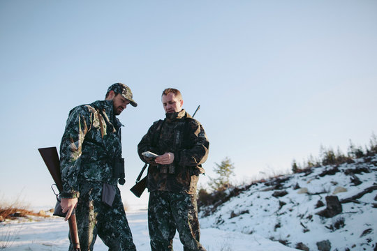 Two men hunting together using gps technology map on mobile phone