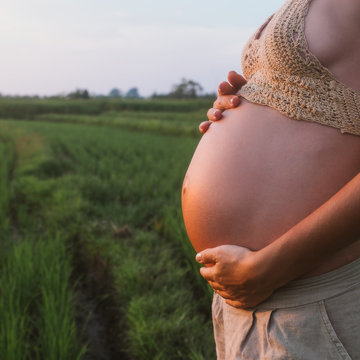Pregnant Woman Holding Her Belly Outside At Sunset In A Green Field