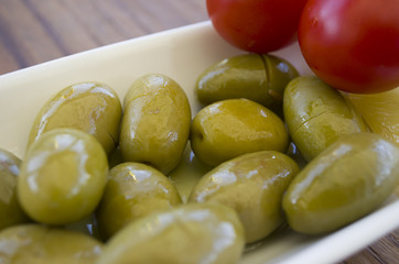 Green olive plate; on a wooden table with lemon slices and cherry tomatoes