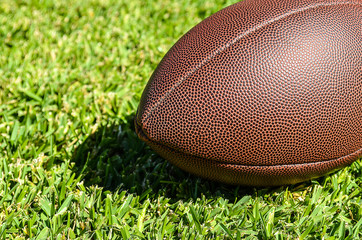 The brown ball for football is displayed on the short green grass. Close up