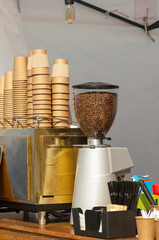 Coffee beans in a grinding machine on the background of paper cups