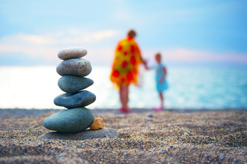 Stones balance and wellness spa concept. Close-up of pebbles stack over blue sea with non recognizable blurred parent and child at background