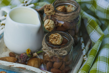 Almonds in the glass, jar with milk on the wooden tray and decorative tubes for drink