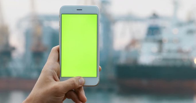 Man male person hand holding using smart phone blur background sea pier port harbour ship yacht background green screen chromakey blank display tapping maritime transport app connection internet