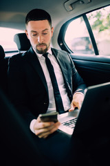 Business Man in rear of the car. Typing text message on cell phone