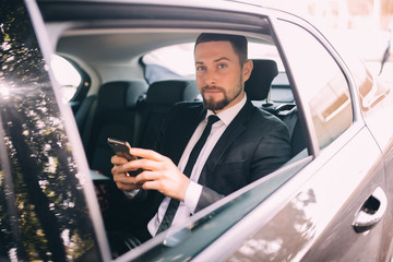 Businessman talking on the mobile phone and looking outside the window while sitting on back seat of car. Male business executive travelling by a car and making phone call.
